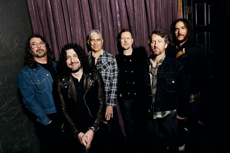 Studio portrait of American rock band Foo Fighters posing together indoors against a dark purple curtain background[cite: 3].